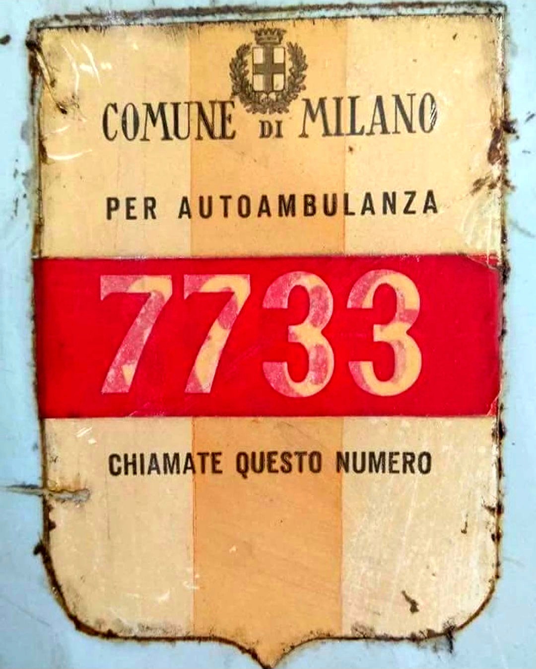 Dettaglio ravvicinato di uno storico contrassegno metallico del Comune di Milano con il numero di licenza per autoambulanza.