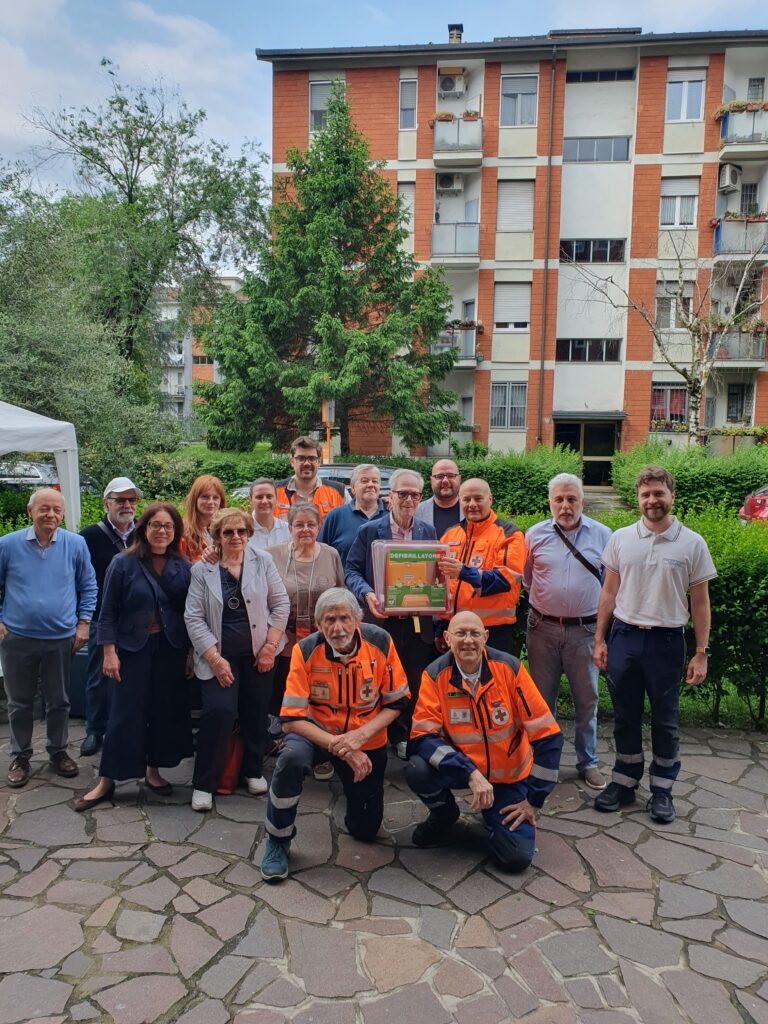 Foto di gruppo all'aperto che unisce i condomini, le autorità locali e i volontari dell'associazione che hanno collaborato all'installazione del DAE con CentoPassiPerLaVita.