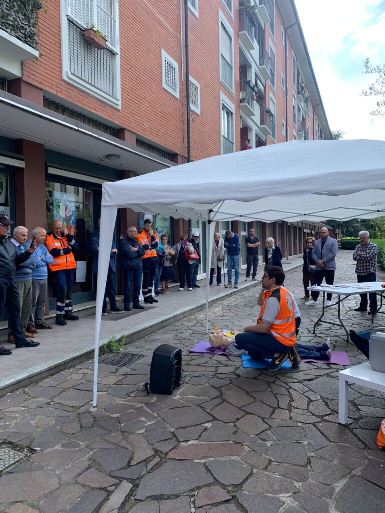 I residenti del quartiere e del condominio disposti in fila assistono con interesse al momento del taglio del nastro e della presentazione del defibrillatore di CentoPassiPerLaVita.