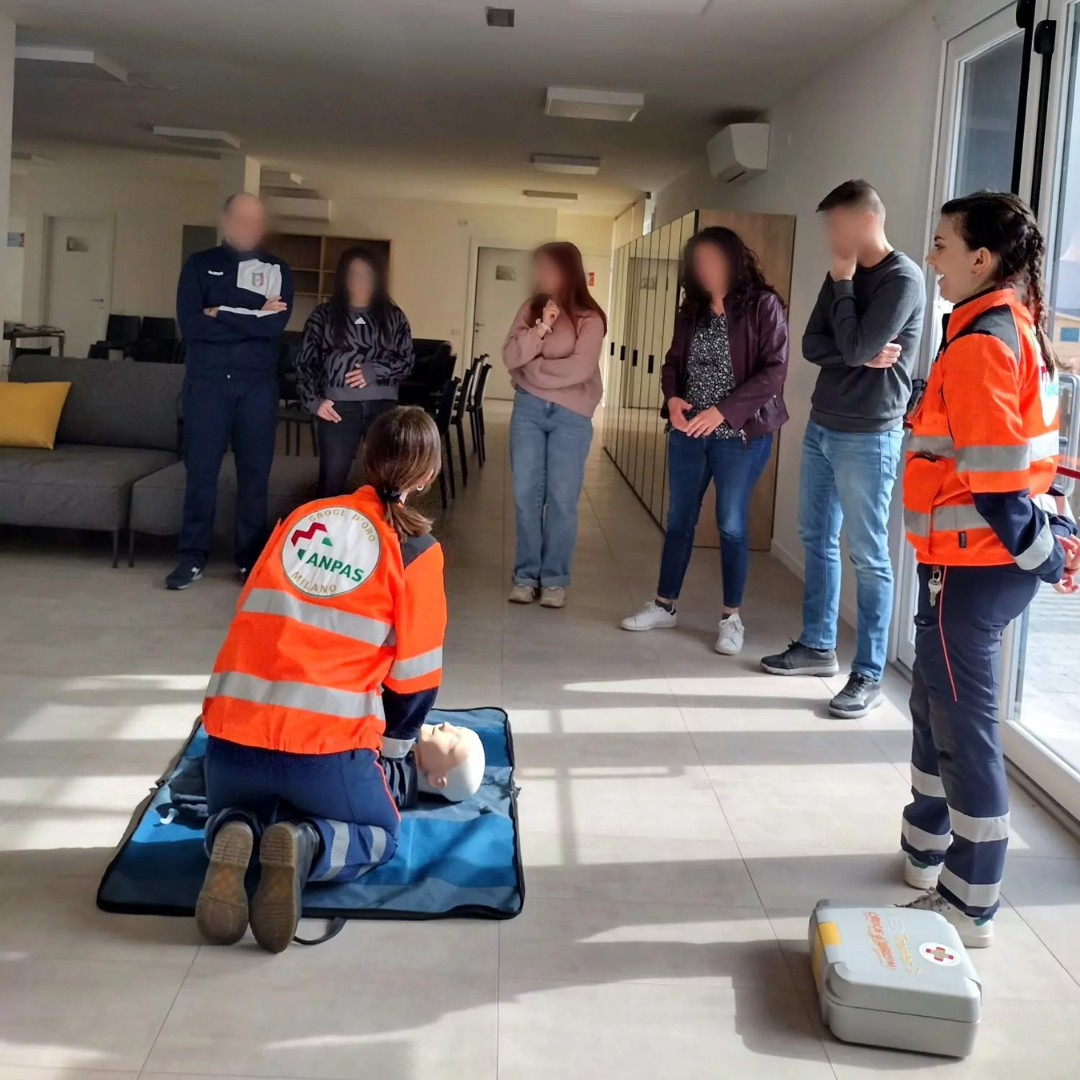 Un'istruttrice della Croce d'Oro Milano esegue una dimostrazione su un manichino da rianimazione davanti a un gruppo di giovani partecipanti durante un corso.