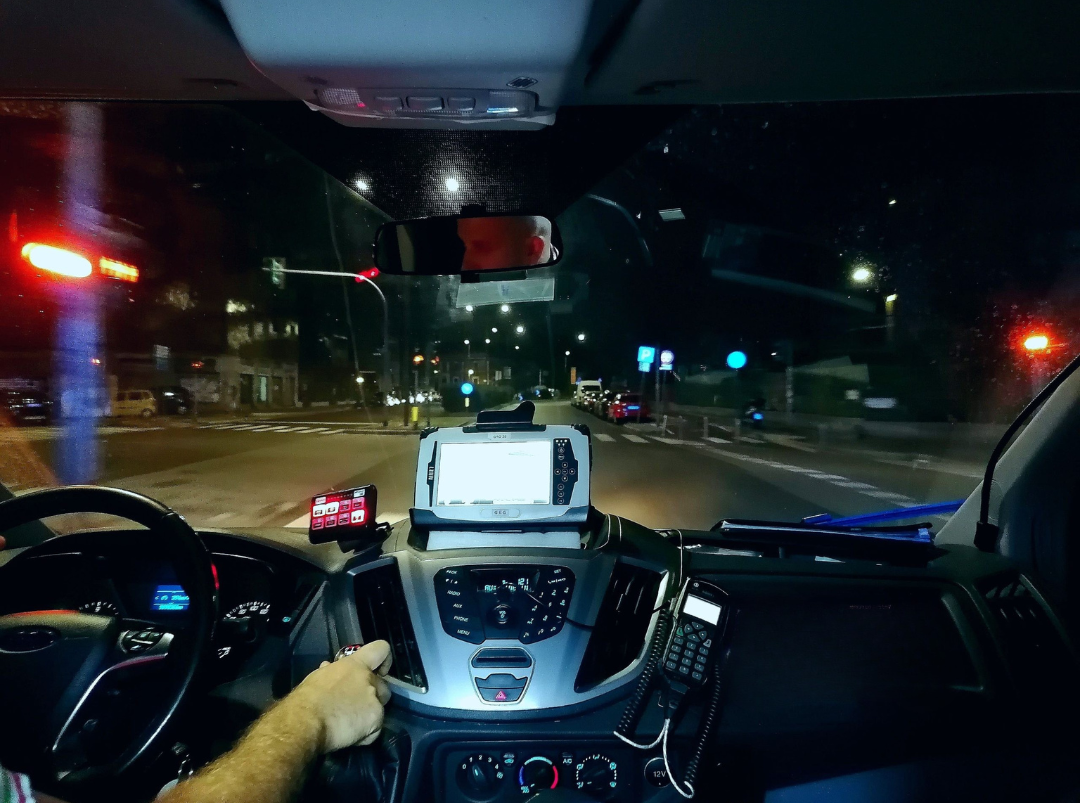Visuale dal posto di guida interno di un'ambulanza della Croce d'Oro in servizio d'emergenza notturno sulle strade illuminate.