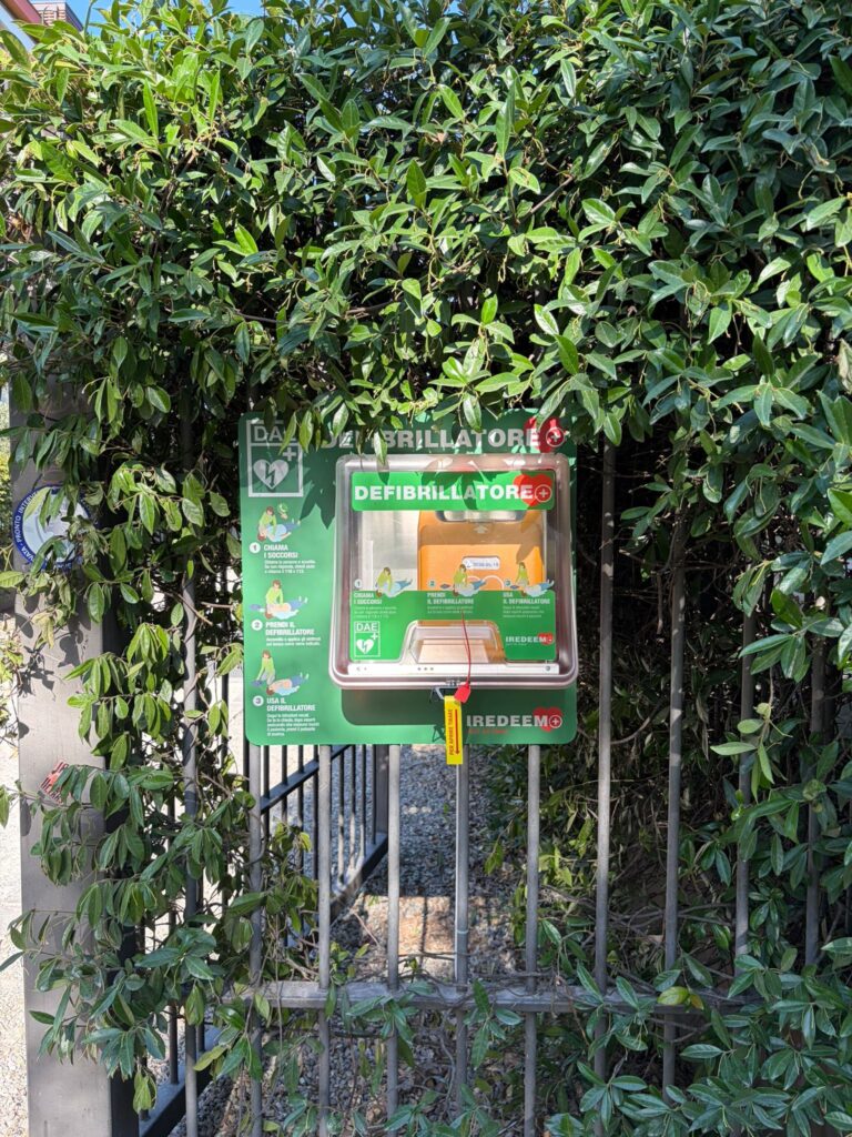 Vista prospettica di un vialetto condominiale con una teca verde salvavita contenente un defibrillatore automatico esterno DAE.